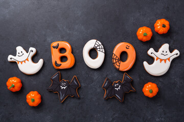 Text BOO from gingerbread cookies with decorative pumpkins and bats on dark stone background....
