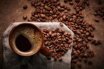 Composition of freshly brewed cup of coffee and roasted coffee beans in bag on brown background