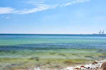 Landscape view of a blue ocean with clear skies on the horizon on a warm summer day. Little waves crash on a quiet calm rocky shore in the mediterranean sea. Panoramic coastline location for tourist