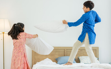 Two people, Indian teenage brother and sister wearing traditional clothes, using pillow, fighting...