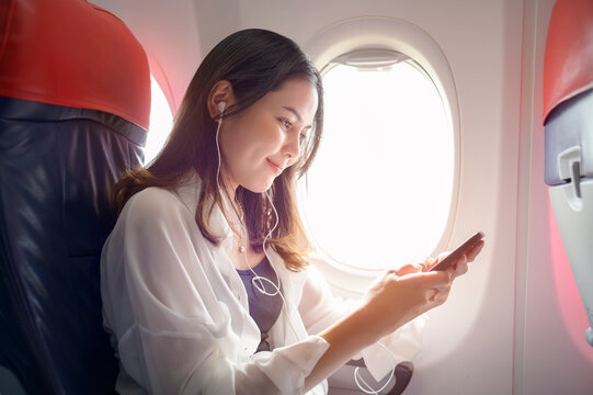 Young beautiful woman is using smartphone on airplane, travel and holidays concept