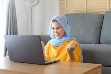 Young happy muslim woman working on laptop in living room at home.