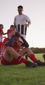 Vertical video of sad biracial football player siting on field