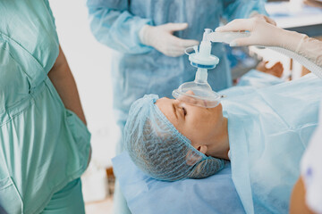 Close up hands of doctor anesthesiologist holding breathing mask on patient face during operation - obrazy, fototapety, plakaty