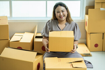  freelance Asian businesswoman sits among boxes of online merchandise, delivering boxes to customers as ordered by customers on their website. Startup Business Ideas and E-Commerce Business