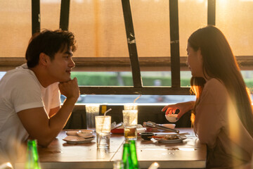 young woman and an Asian man sitting and eating grilled pork or Sukiyaki and Shabu using a Korean stove have dinner together at a Korean-style Shabu restaurant.