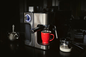 coffee maker and mug milk on a black dark background . making coffee at home