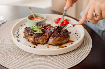 Woman client of the restaurant is eating a medium rare steak. Close up