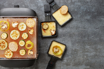Delicious traditional Swiss melted raclette cheese on diced boiled or baked vegetables served in individual skillets. Top view.