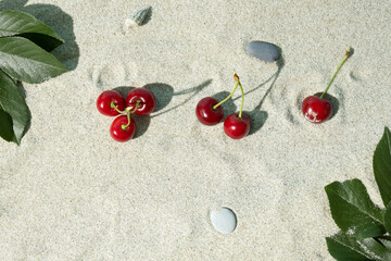 Fresh red organic cherries and green branches on a sandy beach on a hot day. Creative summer concept. Flat lay composition.
