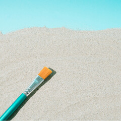 Minimal art creative concept of a paintbrush on the sandy beach and blue background. summer concept with copy space. flat lay view.
