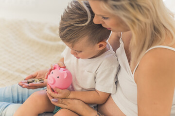 Proud young caucasian mother learning her son how to use a piggy bank. Saving up some coins. Parent...