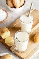 Glasses of powdered vegan potato milk, potato powder, tubers on wooden board on concrete.