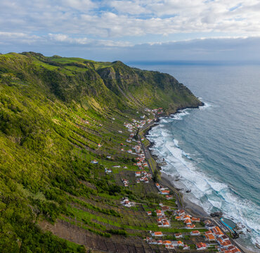 Aerial view of houses along the coastline with terrace fields on the slopes of the cliff overlooking the ocean, Santo Espirito, Azores, Portugal.