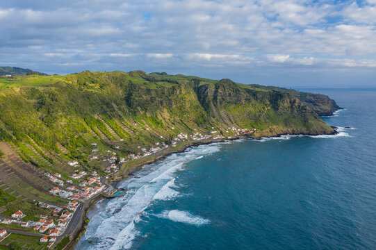 Aerial view of houses along the coastline with terrace fields on the slopes of the cliff overlooking the ocean, Santo Espirito, Azores, Portugal.
