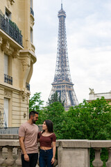 Fototapeta na wymiar Young couple in love looking at each other and hugging on a Paris street with the Eiffel Tower in the background.