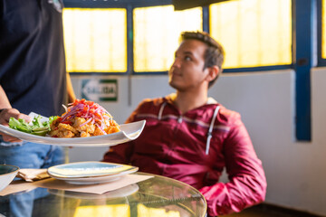 Focus on a waiter serving a dosh of ceviche in a table with clients