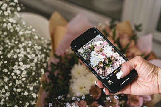 Hands holding phone and taking photo flowers flat lay. Content for social media concept, blogging photos. Happy mothers day.