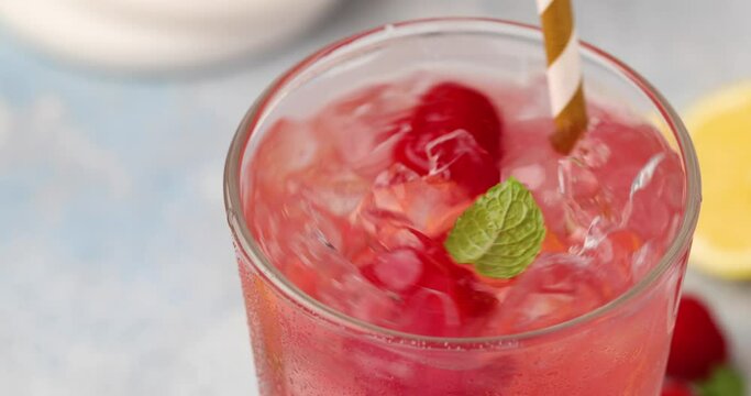 Spring or summer refreshing cold cocktail or mocktail with berries and lemon, raspberry lemonade being stirred with a straw