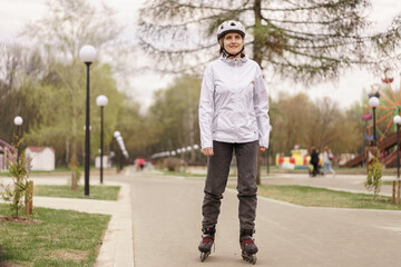 woman wearing a white helmet and white jacketon roller skates at a park © alenaphoto