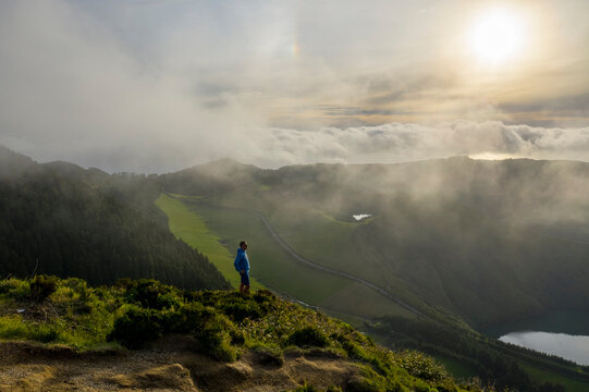 Aerial View of person on the top of the mountain watching Lagoa de Santiago on Miradouro da Boca do Inferno, Sete Cidades, Azores, Portugal.