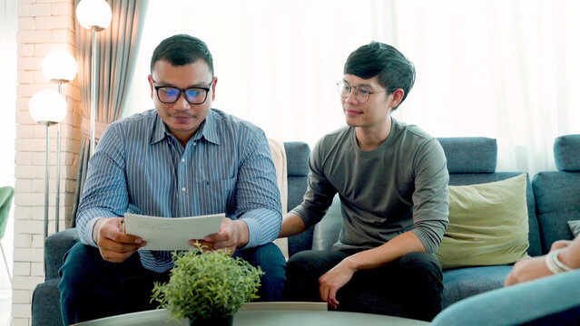 LGBTQ couples chatting on the sofas of their homes looking at the house lease documents as they move in together on the day they both love each other to continue their happily married life.