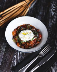 Appetizing dish on a dark wooden table. Vegetable stew with egg.