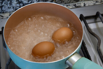 Cooking chicken eggs in boiling water in a light blue saucepan on the stove.