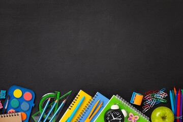 Black chalkboard school background with school supplies and stationery items, empty copy space for text