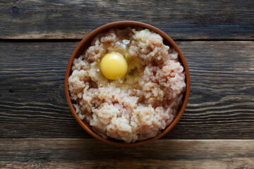 Cooking chicken minced meat with spices and egg in a clay bowl on a wooden table with copy space, top view