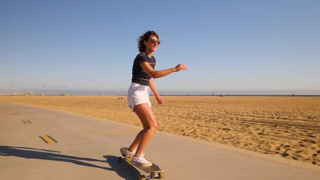 Sporty Young Woman In Sunglasses Dancing And Spinning While Riding Longboard In The Beach Park. - wide, front