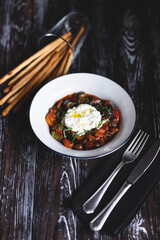 Appetizing dish on a dark wooden table. Vegetable stew with egg.