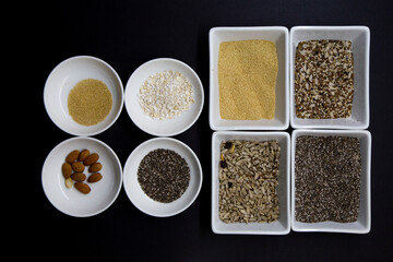 Dark background with white bowls contain healthy seeds for a vegan diet