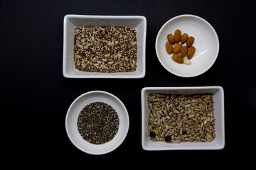 Dark background with white bowls contain healthy seeds for a vegan diet