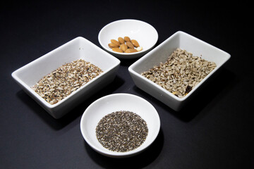 Almonds, chia and other healthy vegan seeds in white porcelain bowls on a black background