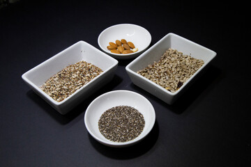 Almonds, chia and other healthy vegan seeds in white porcelain bowls on a black background