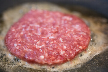 Closeup of a fresh meat burger frying in the frying pan with a small focus. Beef burger.