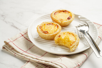 Traditional portuguese vanilla pudding puff pastry pastel de nata on white plate on checkered kitchen towel with a cup of coffee in white porcelain