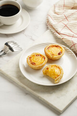 Traditional portuguese vanilla pudding puff pastry pastel de nata on white plate on marble board with a cup of coffee in white porcelain