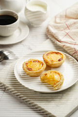 Traditional portuguese vanilla pudding puff pastry pastel de nata on white plate on marble board with a cup of coffee in white porcelain