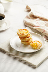 Traditional portuguese vanilla pudding puff pastry pastel de nata stacked on each other on white plate on marble board with a cup of coffee in white porcelain