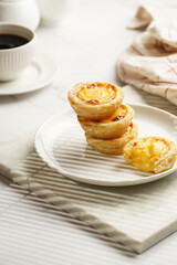 Traditional portuguese vanilla pudding puff pastry pastel de nata stacked on each other on white plate on marble board with a cup of coffee in white porcelain