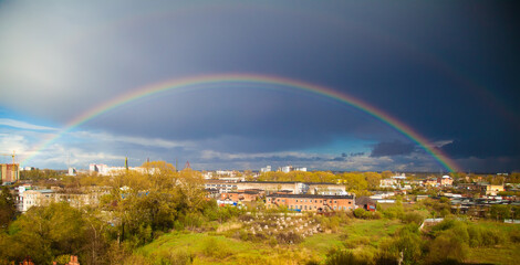 A bright multi-colored rainbow over the city against the background of dark thunderclouds