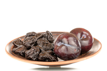 Two fresh black plums and a few prunes on a clay dish, close-up, isolated on a white background.