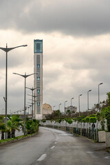 The Great Mosque of Algiers, world's tallest minaret and it's dome, overcast sky and heavy clouds diffusing light on background. Tarmac road with palm trees and city light electric poles on foreground