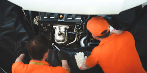 Two male car technician and mechanic checking and repairing engine of car in garage wearing uniform