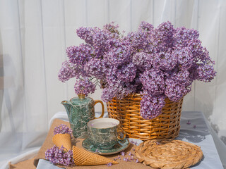 A bouquet of lilacs in a basket and a tea set. Ice cream waffle cones are decorated with flowers. Side view background white