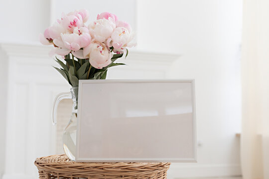 Horisontal frame mockup. Glass vase with a bouquet of pink peonies. Modern fireplace in a Scandinavian interior.