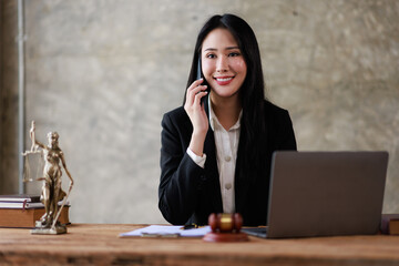 Attractive young lawyer or Businesswoman talking on phone and lawyers discussing contract papers with brass scale on wooden desk in office. Law, legal services, advice, Justice and real estate concept