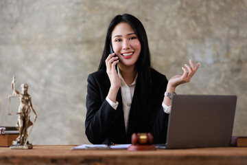 Attractive young lawyer or Businesswoman talking on phone and lawyers discussing contract papers with brass scale on wooden desk in office. Law, legal services, advice, Justice and real estate concept